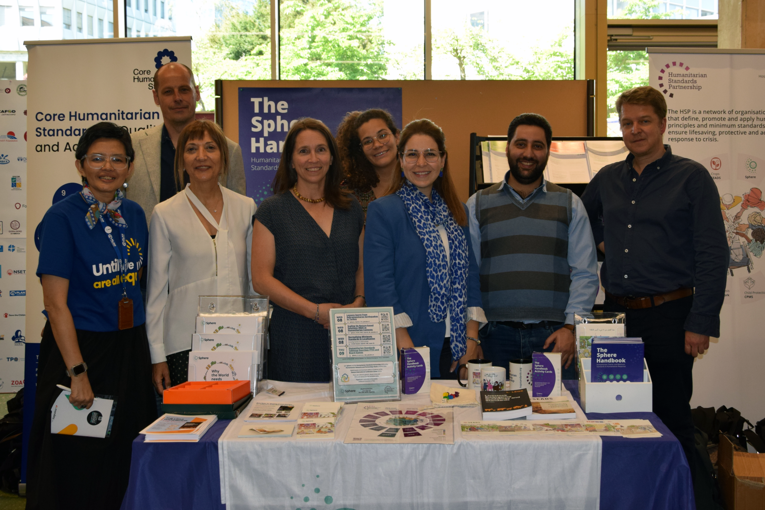 Sphere focal point representatives, members, trainers and staff at Sphere’s HNPW 2024 market stall. From left to right: Vanda, Romain, Zeynep, Felicity, Amanda, Aya, Yaman and William.